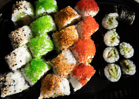 Zbliżenie bułek sushi z czerwonym kawiorem, łososiem, tuńczykiem i awokado izolowane na czarnym tle. Pyszne tradycyjne japońskie jedzenie z bułkami soshi.