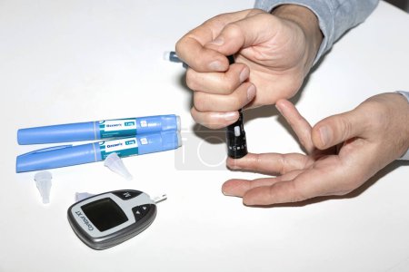 Foto de Hombre diabético midiendo el nivel de azúcar en sangre. Análisis de sangre para diabetes y pluma inyectable con insulina Ozempic. Dinamarca - 10 de febrero de 2024 - Imagen libre de derechos