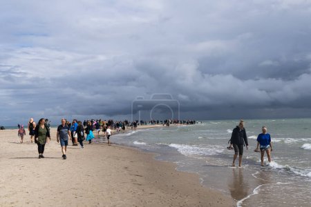 Foto de Muchas personas caminan a lo largo de la orilla del mar o el océano en un día nublado tormentoso. Skagen, Dinamarca - 25 de septiembre de 2023. - Imagen libre de derechos