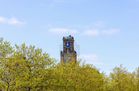 Tower with a clock on which 12 o'clock against of the sky and green foliage. High quality photo