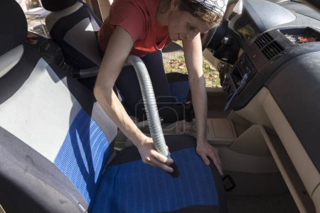 Téléchargez les photos : Mid Adult Femme Nettoyage à l'intérieur de sa voiture avec un aspirateur - en image libre de droit