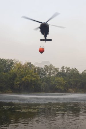 Téléchargez les photos : Chopper de la Force aérienne militaire slovaque utilisé à des fins de lutte contre les incendies dans un incendie à grande échelle dans Karst slovène - Ici chargement de l'eau Forme Vipava River - en image libre de droit