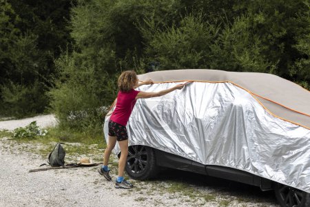 Photo for Woman Hiker Putting on Her car an Anti Hail Protection Cover over Her car Before Leaving - Royalty Free Image