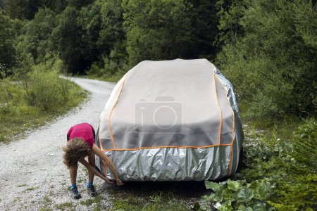 Frau legt vor längerer Wanderung Hagelschutzhülle über ihr Auto