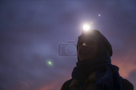 Téléchargez les photos : Portrait rêveur d'une randonneuse avec phare au crépuscule Regardant dans le ciel des ténèbres et des étoiles - en image libre de droit