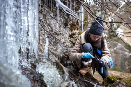 Foto de Ambientalista mujer adulta recogiendo muestras de agua congelada para la contaminación futura Análisis comparativo en invierno Wilderness - Imagen libre de derechos