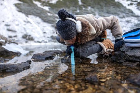 Foto de Experta en supervivencia femenina que bebe agua a través de un carbono Filtro de plata desde un lago semicongelado en las altas montañas de los Alpes europeos - Imagen libre de derechos