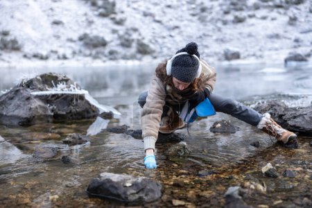 Foto de Mujer bióloga recogiendo muestras del entorno de un lago de montaña en invierno - Imagen libre de derechos
