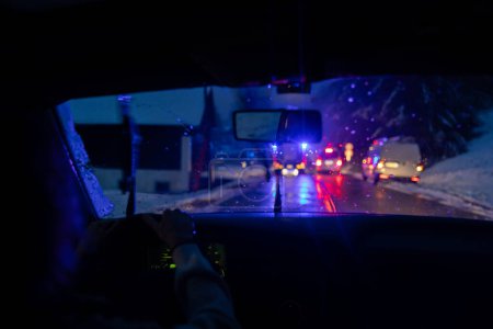 Téléchargez les photos : Vue à travers le pare-brise d'une voiture révèle une scène d'accident de la circulation avec clignotement de la police bleue et des feux d'ambulance de premiers soins rouges, capturant l'urgence et les défis des routes glissantes d'hiver - en image libre de droit