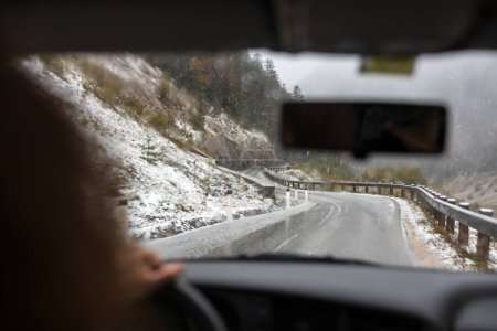 Téléchargez les photos : Vue au-dessus de l'épaule d'un conducteur adaptable confronté à des routes traîtresses couvertes de neige, traversant un relief glacé - en image libre de droit
