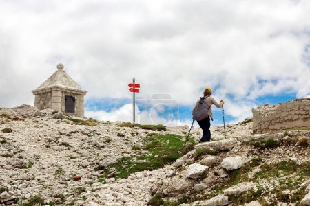 Téléchargez les photos : Femme adulte randonneur atteignant le sommet d'une montagne dans les Alpes juliennes lieu de la Première Guerre mondiale et austro-hongroise Monument aux soldats tombés et courageux - en image libre de droit
