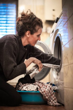 Foto de Mujer adulta poniendo la lavandería en la lavadora en el baño doméstico - Imagen libre de derechos