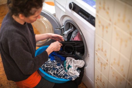 Foto de Mujer adulta sacando la ropa de la lavadora en el baño doméstico - Imagen libre de derechos