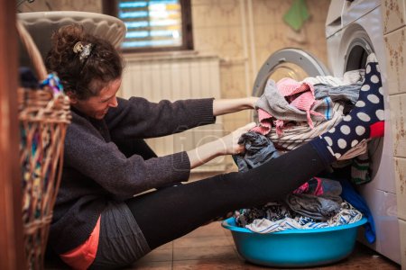 Foto de Mujer adulta luchando por la lavandería con la lavadora en el baño doméstico - Sacando la ropa con peludo - Imagen libre de derechos