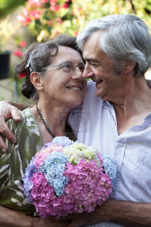 Photo for Senior Wife and Senior Man Caucasian Couple,  40+ years of True Love. Graced by Genuine Smiles in a Garden. Timeless Togetherness, Colorful Flowers, Embracing Enduring Joy - Royalty Free Image