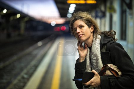 Foto de Mujer guapa viajera esperando un tren en la plataforma de una estación de tren en Italia en la madrugada - Imagen libre de derechos