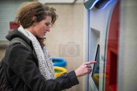 Erwachsene Frau nutzt elektronisches Fahrkartensystem am Bahnhof, um frühmorgens ein Zugticket zu kaufen