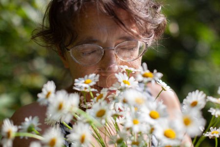 Seniorin duftet mit geschlossenen Augen einen Strauß Gänseblümchen im Freien