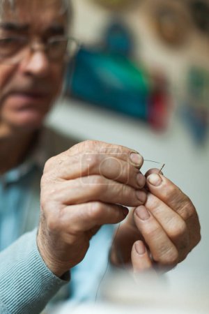 Photo for Old Man With Glasses Trying To Put Thread trough Hole of Sewing Needle - Royalty Free Image