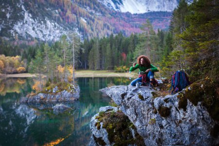 Foto de Senderismo Comida caliente Alegría para una mujer adulta Senderista en un lugar rocoso cerca de un lago de montaña - Imagen libre de derechos