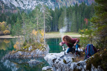 Foto de Cabello rizado caucásico mediana mujer adulta excursionista preparándose un café italiano cerca de un lago en las montañas - Imagen libre de derechos