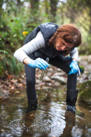 Foto de Bióloga mujer caucásica adulta que trabaja en el control de campo para detectar contaminación mecánica o biológica visible en una corriente de agua - Imagen libre de derechos
