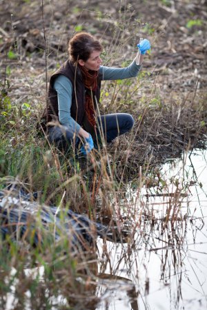 Foto de Bióloga mujer adulta que trabaja en el control de campo y la recolección de muestras de agua posiblemente contaminada de plaguicidas - Imagen libre de derechos