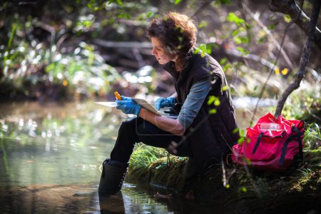 Foto de Investigadora de biología de mujeres adultas que recopila datos sobre la contaminación del agua en el campo en un entorno forestal rural - Imagen libre de derechos