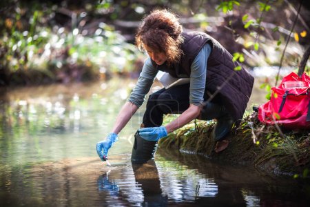 Mittlerer Erwachsener Biologe sammelt Wasserproben für weitere Untersuchungen aus einem Wasserlauf auf dem Land
