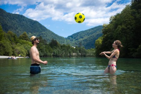 Téléchargez les photos : Touristes de couple adultes jouant un jeu de volley-ball rafraîchissant amusant à Alpine River Vacances d'été - en image libre de droit