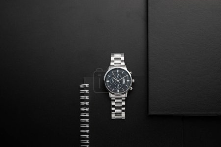 Foto de Cuaderno negro con el reloj de plata sobre un fondo negro - Imagen libre de derechos