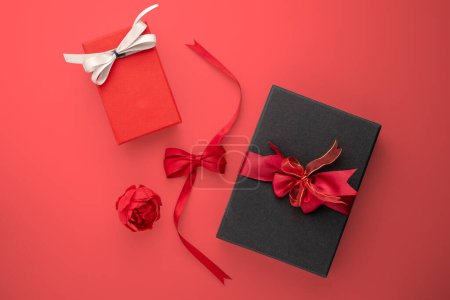 Foto de Cajas de regalo negras y rojas con cintas y rosa sobre una mesa roja. - Imagen libre de derechos