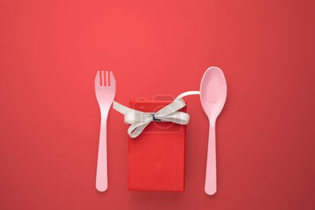 Téléchargez les photos : Fourchette rose et cuillère avec une boîte cadeau avec ruban rose sur fond rouge - en image libre de droit