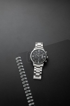 Foto de Cuaderno negro con el reloj de plata sobre un fondo negro - Imagen libre de derechos