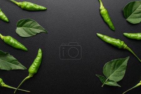 Foto de Chiles verdes frescos y hojas sobre fondo negro - Imagen libre de derechos