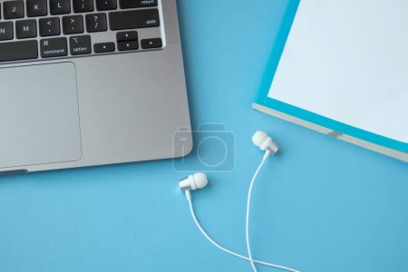Photo for Earphones and  white book with laptop  on blue background - Royalty Free Image
