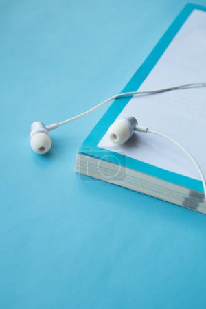 Photo for Top view of white earphones and notebook on blue background with copy space. Flat lay. Audio book concept - Royalty Free Image
