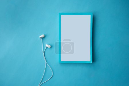 Foto de Vista superior de auriculares blancos y portátil sobre fondo azul con espacio para copiar. Acostado. Concepto de audio libro - Imagen libre de derechos