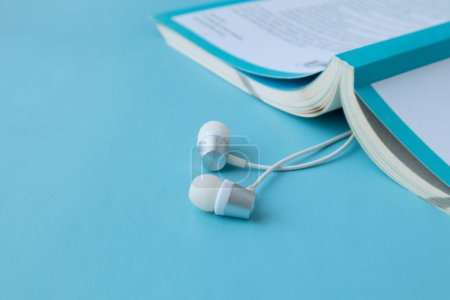 Photo for Top view of white earphones and notebook on blue background with copy space. - Royalty Free Image