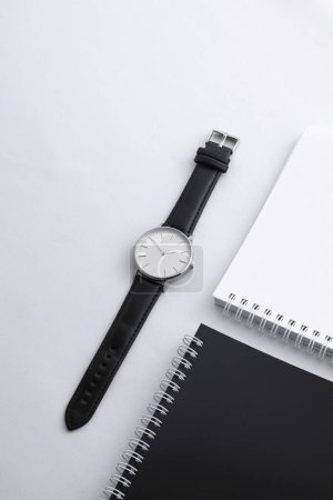 Foto de Reloj de cuero negro en escritorio blanco con cuadernos en blanco y negro - Imagen libre de derechos