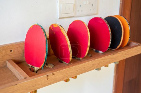 Colorful ping pong paddles placed in brown wooden shelf.