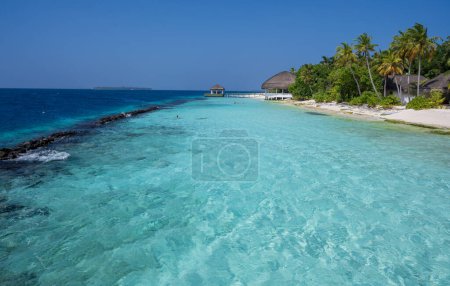 Sea lagoon and coast of tropical island. Tropical houses, sandy beaches and dense green forest. Blue sky.