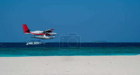 Das Wasserflugzeug fliegt tief über dem Meeresspiegel am Sandstrand entlang. Blauer Himmel.