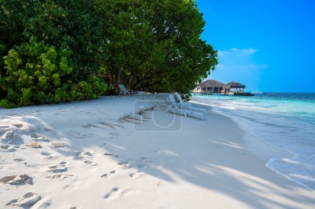 A sandy beach near a dense tropical forest. In the background is a tropical building over water. Blue sky.