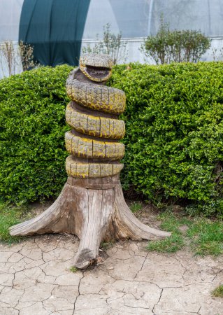 Wooden sculpture of snake wrapped around tree trunk.