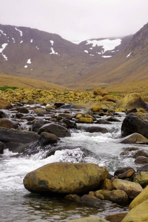 Stream tumbling over rocks in the foreground with desolate mountain slopes in the background in the Tablelands region of Gros Morne National Park on Newfoundland s western coast