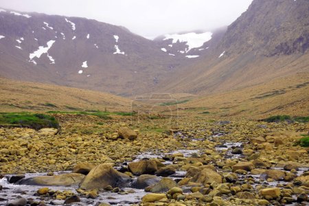 Mountain valley with grass and a stream backed by snow-covered peaks in the Tablelands on Newfoundland's western coast