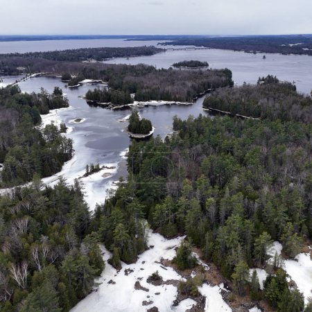 Small forested islands in the Ottawa River in late winter surrounded by ice and open water