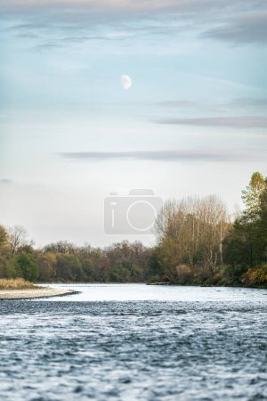Foto de La luna con algunas nubes en el cielo y el río Mura fluyendo en el suelo. - Imagen libre de derechos