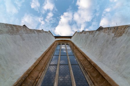 Looking up at a curch facade with a window and cloudy sky